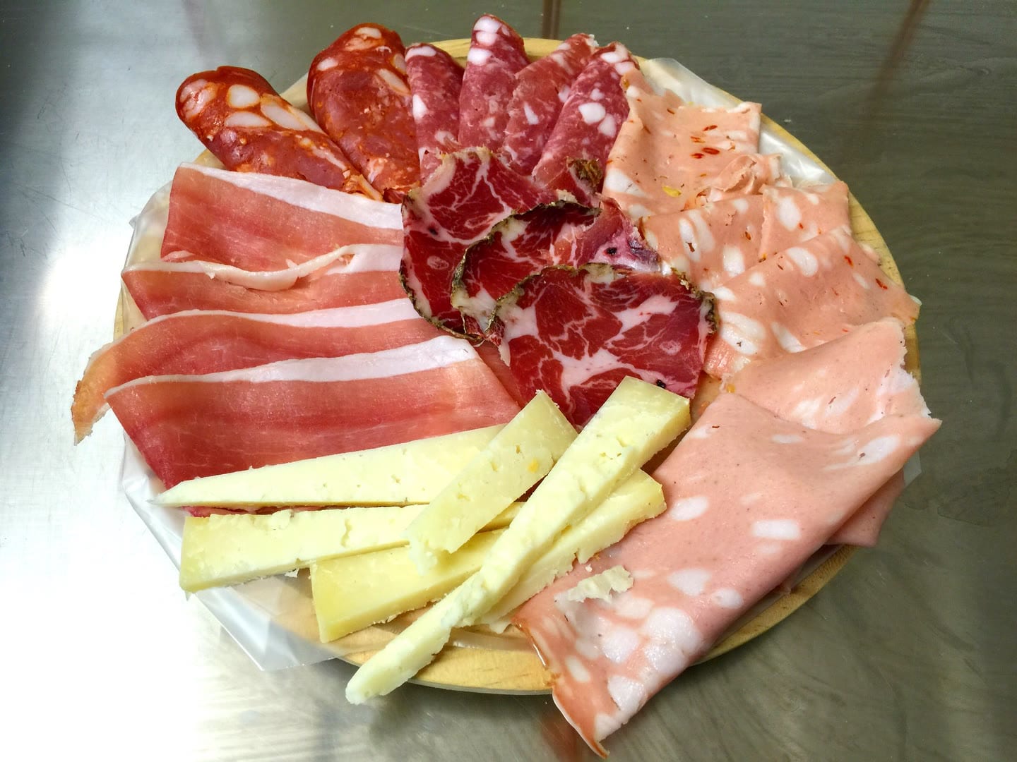 Un tagliere tondo di legno con prosciutto crudo, salame, coppa, mortadella e scaglie di formaggio.